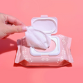 Hand pulling a wet wipe from a white wipes packet on a pink background